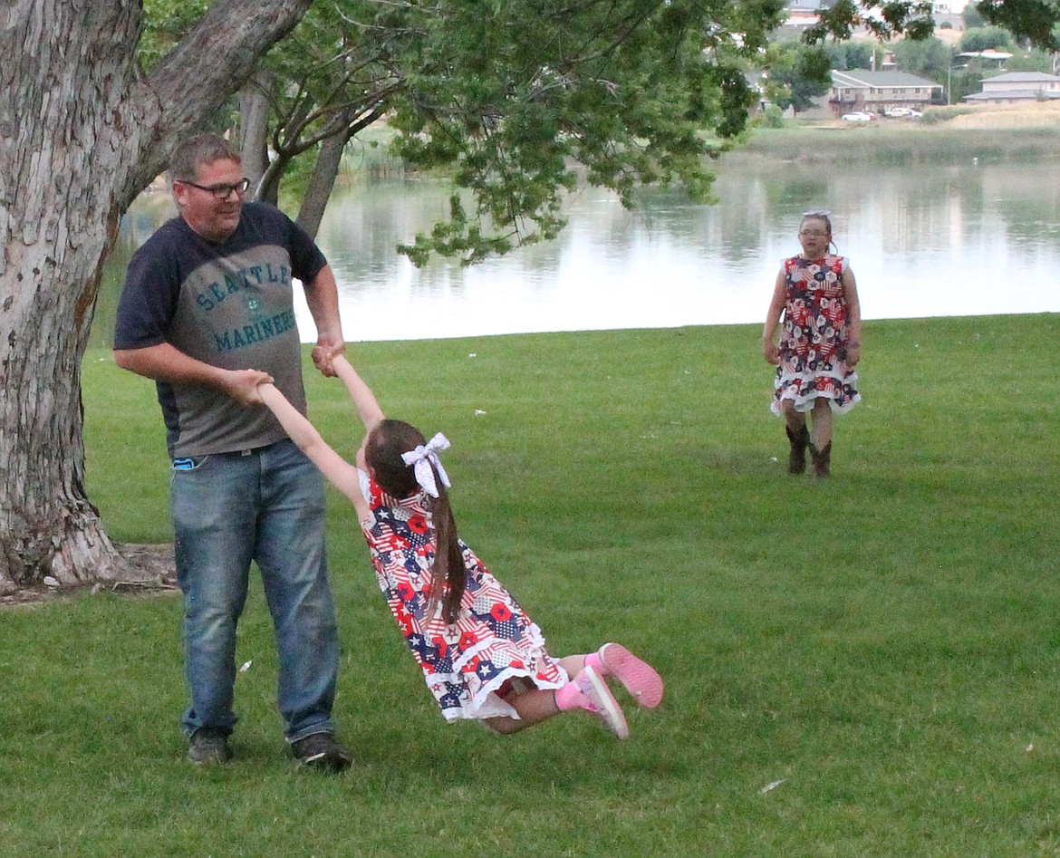 John Thompson of Basin City swings his daughter Shaylee Thompson around while her sister Brieley catches up at McCosh Park during Moses Lake Freedom Fest.