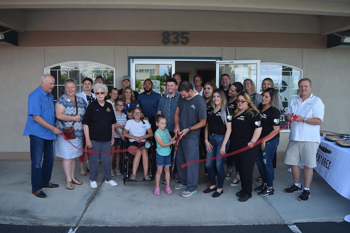 Jon Dickson hands the Moses Lake Chamber of Commerce’s giant scissors to his youngest daughter Roxy, 7, after cutting the ribbon on his new business, Professional Dentures, at 835 W. Colonial Ave. Suite 103, in Moses Lake, on Wednesday. Dickson, who also has an office in Wenatchee, said he also does oral surgery under general anesthesia.