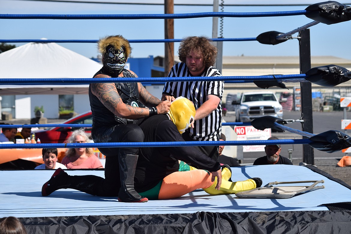 Black Danger slowly unlaces the mask of his opponent, El Quete, as referee Garrett Ambrose looks on, during a bout on Saturday at the grand opening of EDUBB C/S in Moses Lake.