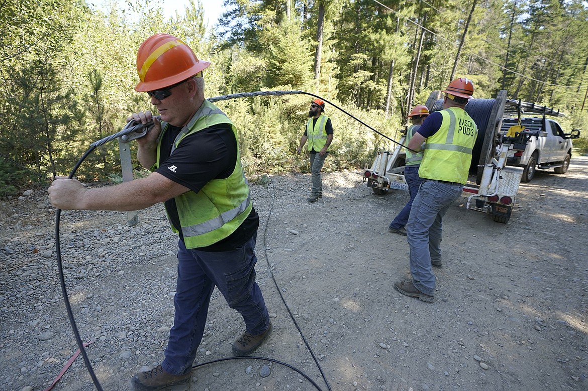 Carl Roath, left, a worker with the Mason County (Wash.) Public Utility District, pulls fiber optic cable off of a spool, as he works with a team to install broadband internet service to homes in a rural area surrounding Lake Christine near Belfair, Wash., on Aug. 4, 2021. (AP Photo/Ted S. Warren, File)