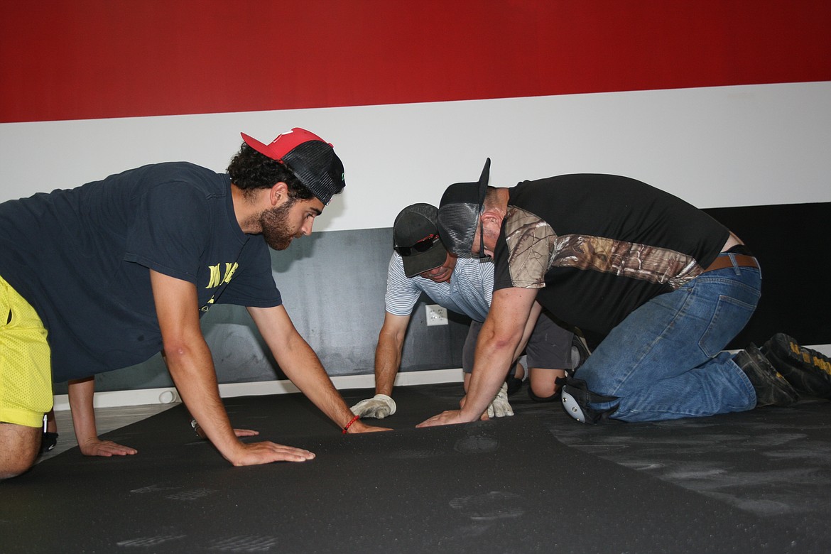 (From left) Jonathan Garza II, Oscar Garza and Jonathan Garza lay flooring as part of rebuilding Jab Fitness, the family business.