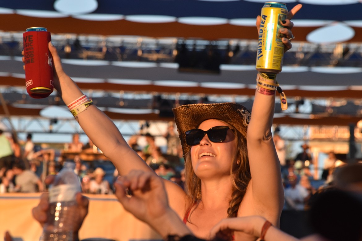 A fan holds up her drinks during one of the performances as the sun sets at the Gorge.