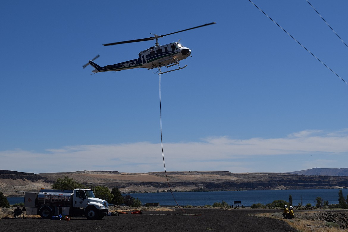 A helicopter takes off from the gravel lot in front of the fire station in Vantage. The line attached to the bottom of the aircraft is attached to a bucket used to pull water from the nearby Columbia River to dump on the fire.