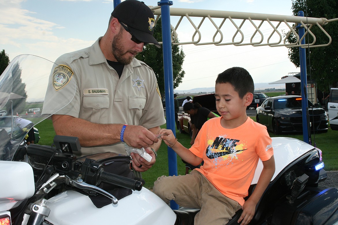 Grant County Sheriff’s Department deputy Stormy Baughman (left) gives a stick-on badge to Christopher Diaz (right) at National Night Out in Quincy, sponsored by the Quincy Police Department.