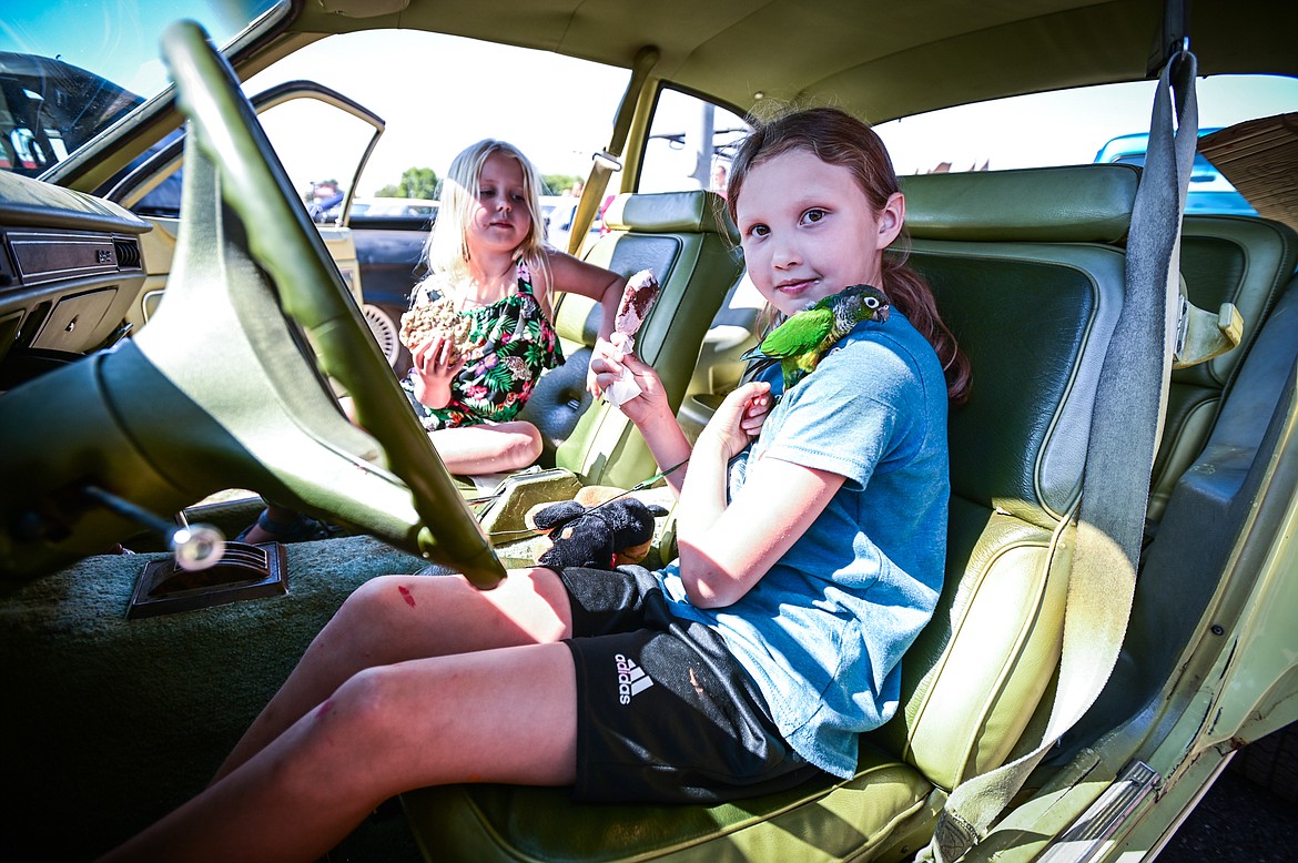 Luna Burton, right, and Savannah Abramovitz eat ice cream while Luna plays with Molly, a yellow-sided green cheek conure inside Savannah's father's 1975 Mercury Bobcat at the Evergreen Show 'N Shine car show at Conlin's Furniture on Saturday, Aug. 6. (Casey Kreider/Daily Inter Lake)