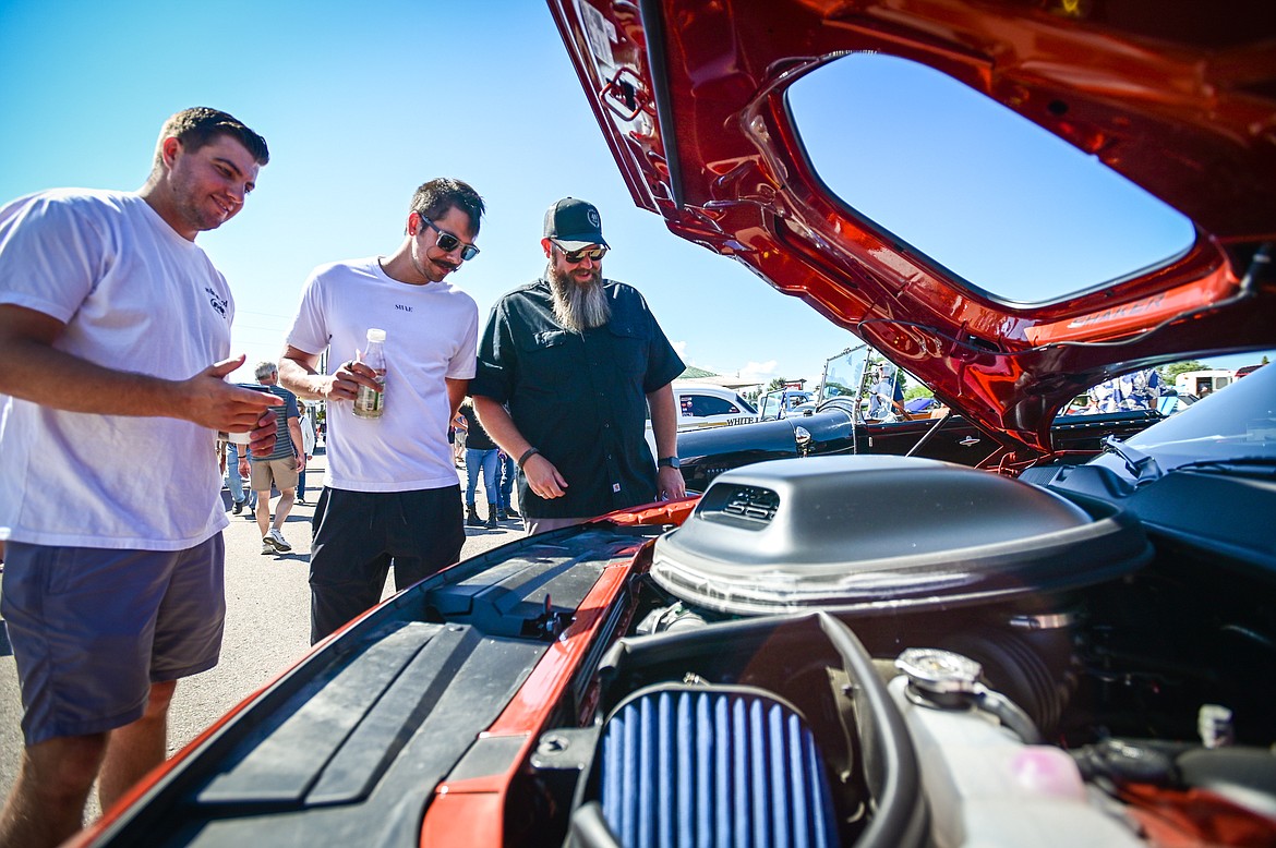 From left, Kevin Croteau, Colton Hermosillo and Chris Martin look under the hood of Croteau's 2021 Dodge Challenger RT Scatpack at the Evergreen Show 'N Shine car show at Conlin's Furniture on Saturday, Aug. 6. (Casey Kreider/Daily Inter Lake)