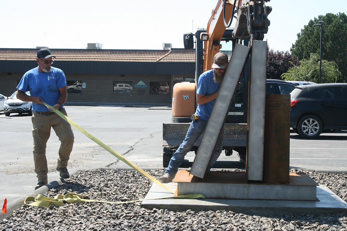 Steve Miers (left) and Brandon Miers (right) remove the straps during the Monday installation of a sculpture outside the Moses Lake School District Learning Services Center.
