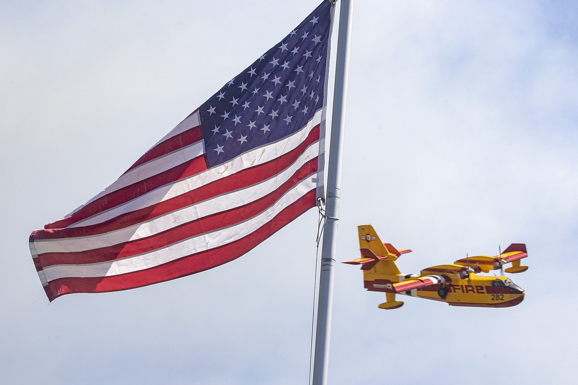 A scooper plane flies by a U.S. flag while tending to the Elmo 2 Fire in Lake County. (Rob Zolman/Lake County Leader)