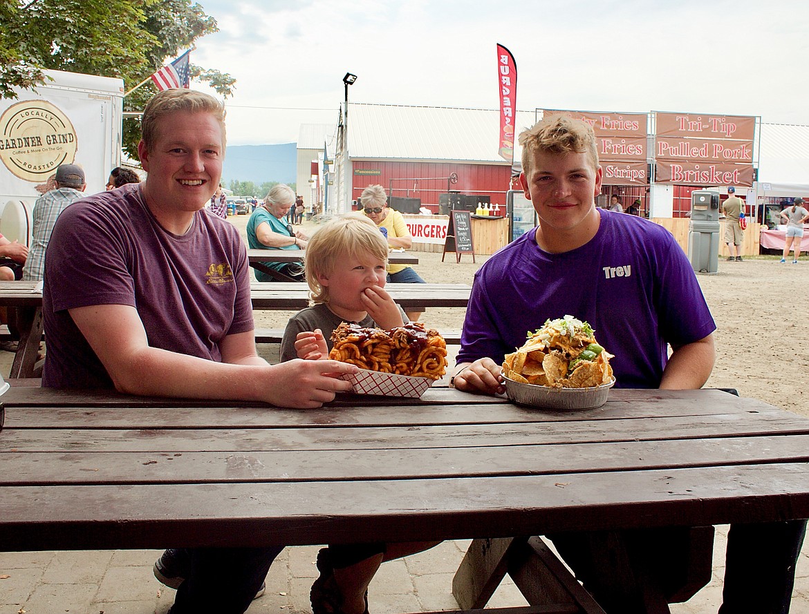 (left right) Harmon and Porter Newhouse with Trey Bateman sample some of the food available at the 102nd Boundary County Fair.