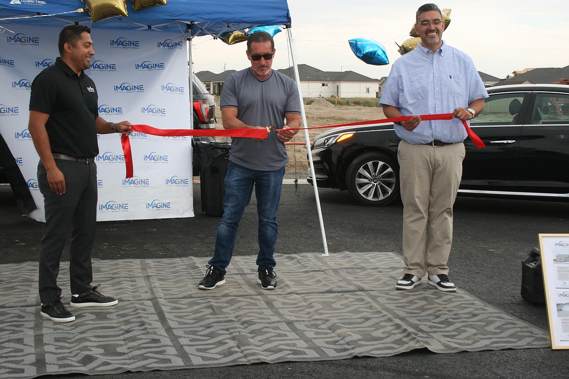 Developer Angel Garza (center) cuts the ribbon for the fourth phase of the Sandhill Estates development in Othello. Miguel Velasquez of Envoy Mortgage (left) and Jessie Dominguez of Imagine Realty (right) hold the ribbon.