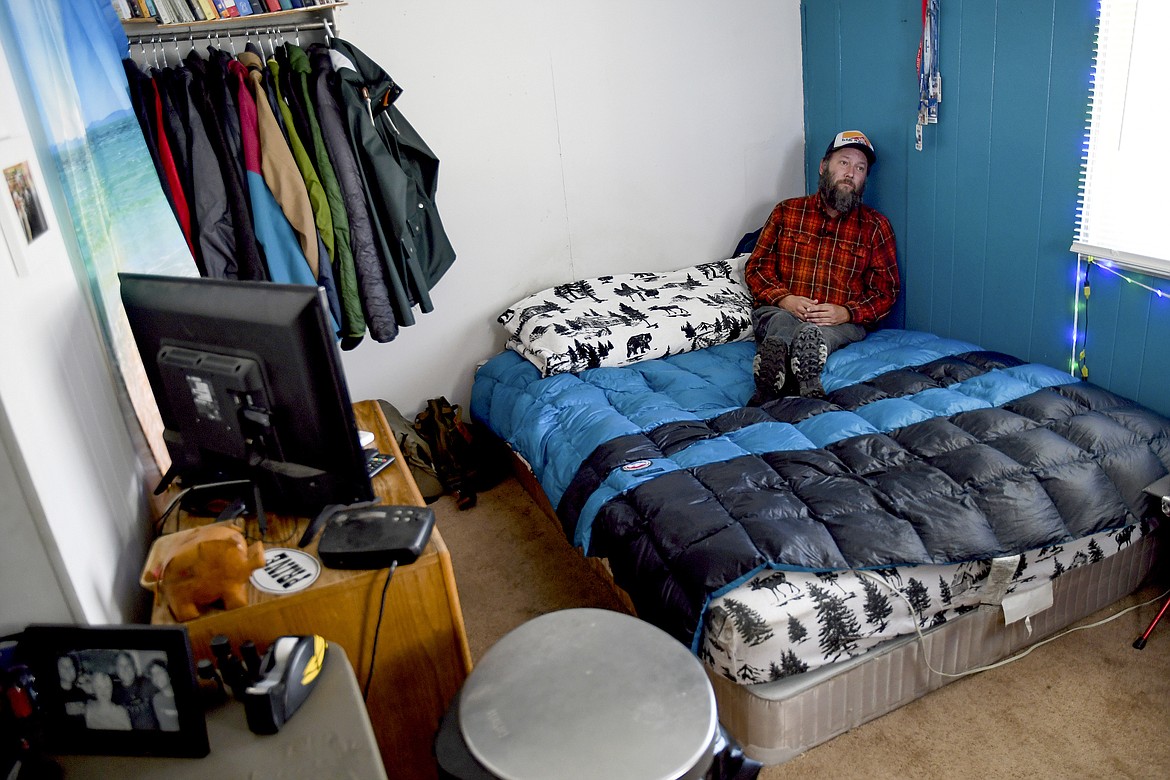 Sean Bailey sits in his bedroom, Thursday, Aug. 4, 2022, in Steamboat Springs, Colo. Bailey, who moved to Steamboat Springs in 2019, has been on a waitlist for three years to get one of Steamboat's affordable housing apartments. He says the 12-foot-by-12-foot space serves as his living room, dining room, den and office. (AP Photo/Thomas Peipert)