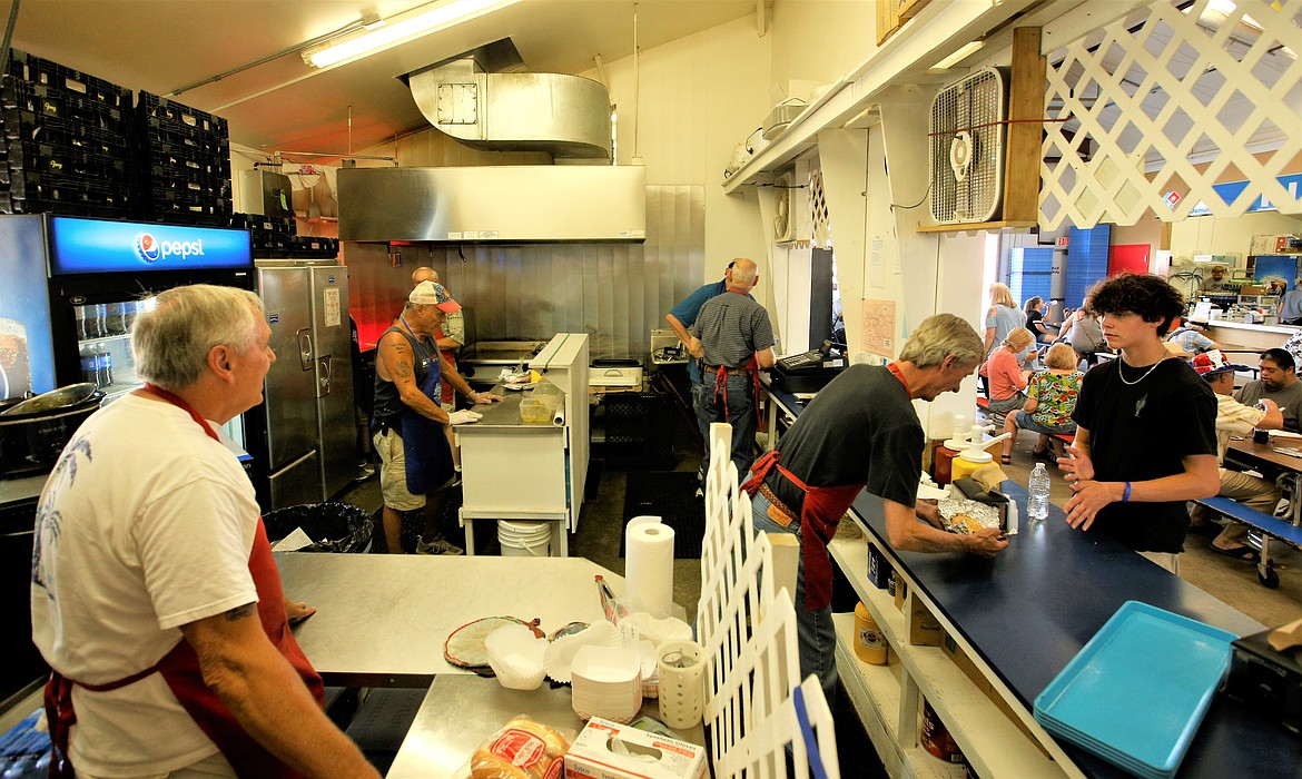 Ron Hartman helps a customer at the counter while other members of the Knights of Columbus work in the Dog House kitchen in the Food Court at the North Idaho State Fair on Tuesday.