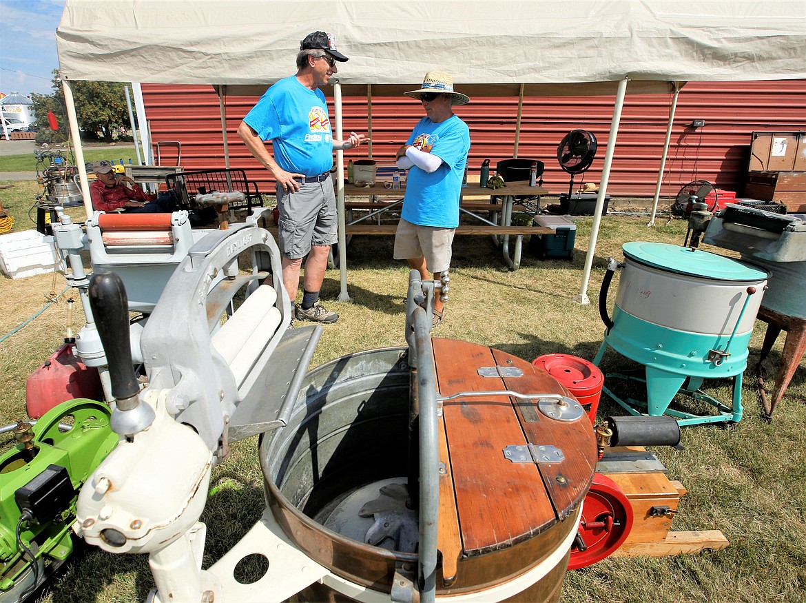 Roger Hahn, left, and Dennis Dingman stand behind a century-old washing machine as they chat in the vintage agricultural equipment area of the North Idaho State Fair on Wednesday.