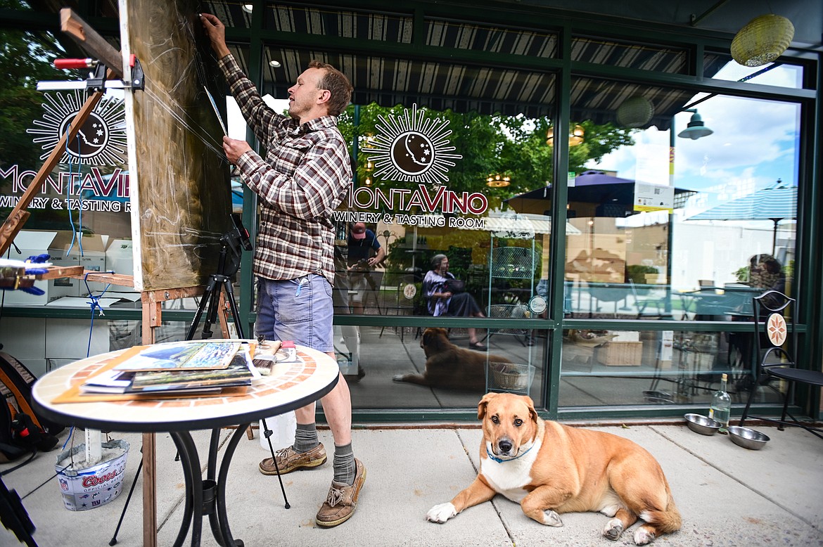 Artist Haakon Ensign works on a rendition of a Clarence Rundell mural with his dog Lucky for the Kalispell Downtown Association and KALICO Art Center's Downtown Art Challenge on Saturday, Aug. 27. Ten artists each referenced a different Clarence Rundell mural that Rundell painted in 1936 in what is now Rocky Mountain Outfitter on Main Street in Kalispell. The paintings will be hung up and on view in  several downtown businesses from Aug. 31 to Sept. 8, during which time all of the paintings will be up for auction on the following online platform: https://app.galabid.com/kdachallenge/items. (Casey Kreider/Daily Inter Lake)