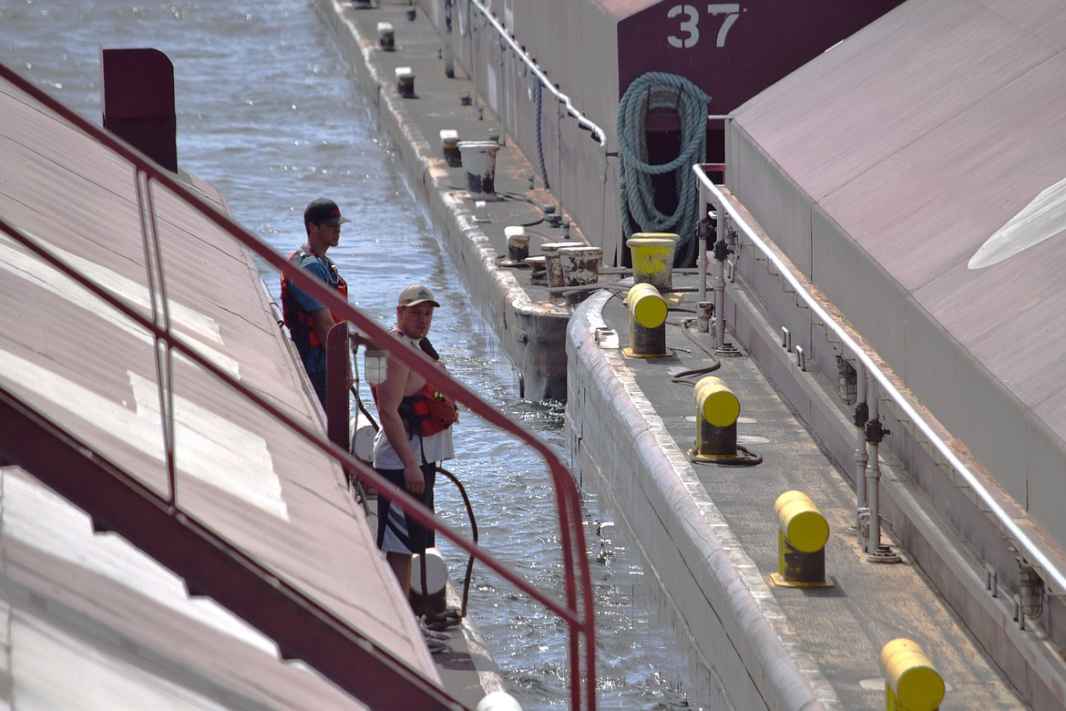 Deckhands Sean Malloy, front, and trainee Colby Glaze stand on the edge of a barge as the tugboat Lincoln edges toward other barges, part of the process of building a tow.