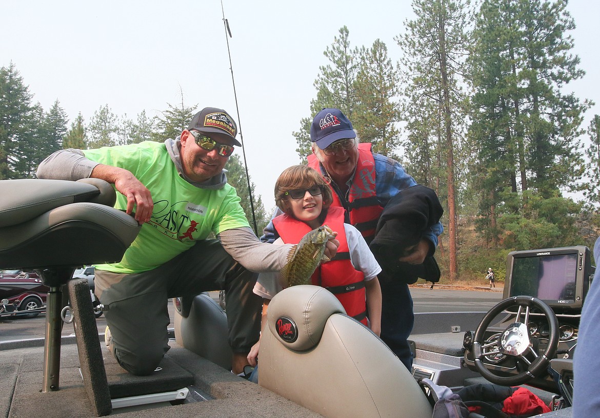 Tanner Sams, 12, of Rathdrum, and his grandpa, Tim Clements, enjoy showing off a smallmouth bass, held by Lakeland Middle School Vice Principal Harrison Bertsch, during the C.A.S.T. for Kids event Sunday morning in Post Falls.