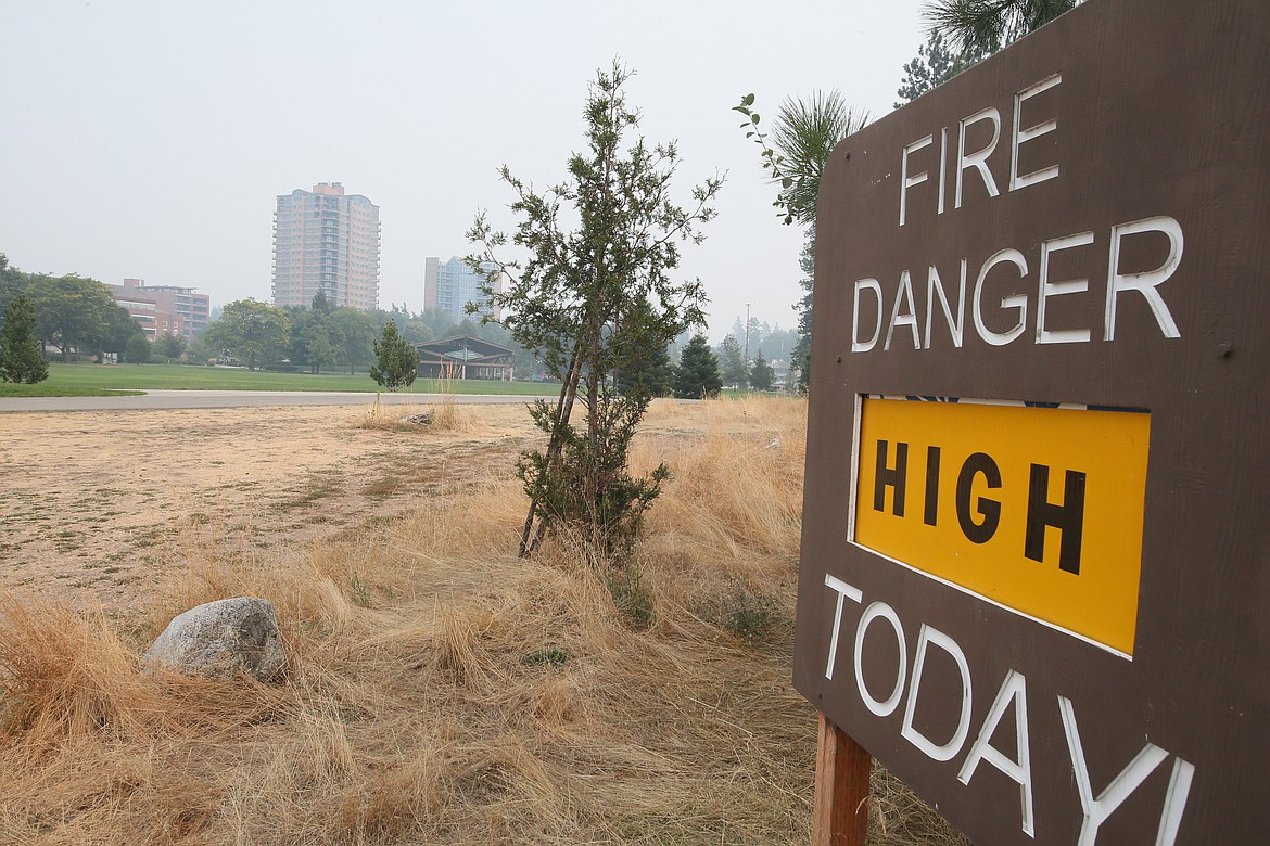 The sign at a Tubbs Hill trail entrance reminds that fire danger is "high" as smoke obscures buildings Monday in downtown Coeur d'Alene.