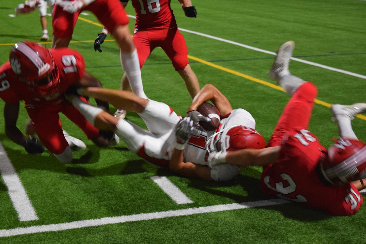 Trojan Luke Pertek (11) hits the grass and clasps the ball after being taken down by Ashton Zabriskie (19) and Sabastian Larzlier (31) during Friday's game.