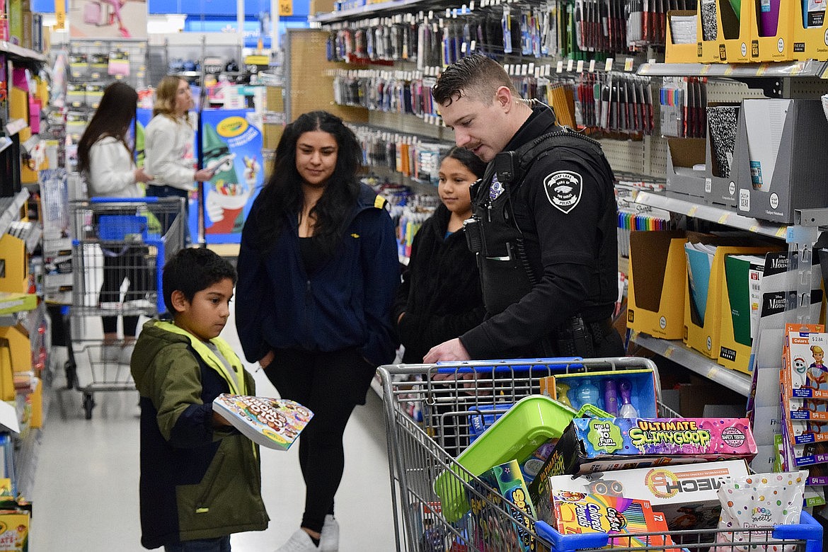 Zack Rodriguez, 6, left, holds a coloring book, while his aunt Angelica Rodriguez, sister Lidia Rodriguez, 9, and Soap Lake Police Department Officer Jeff Gallaher look on at the 2021 Shop with a Cop.