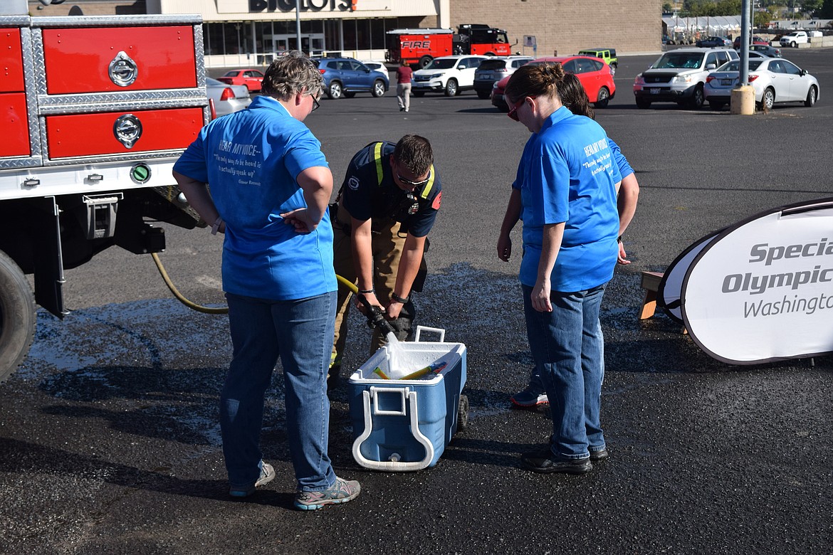 A Moses Lake Fire Department firefighter refills a cooler with water to “re-arm” Special Olympians and others during the “Fire & Cop on Top” fundraiser in Moses Lake on Friday.