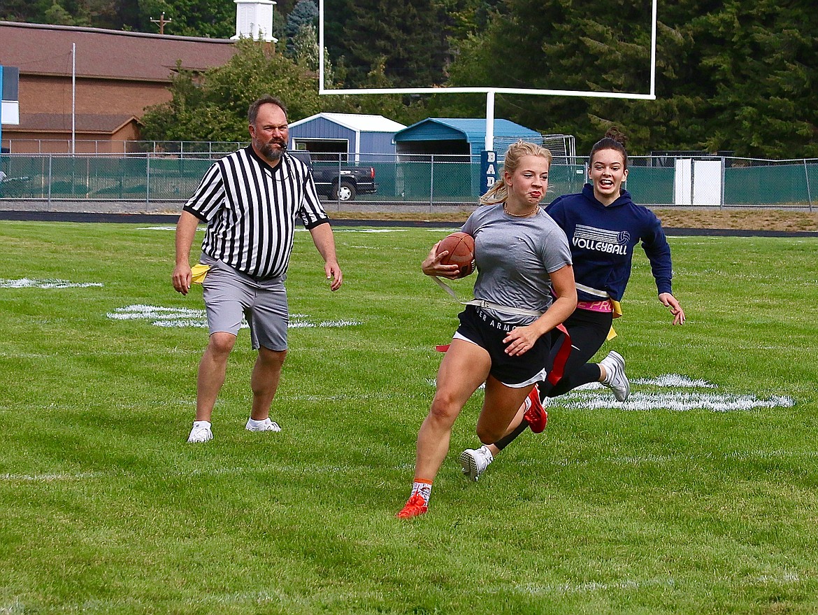At powder puff football, Lindsey Onstott runs the ball for the juniors and is chased down by a sophomore player. Football Coach Travis Hinthorn (left) refs the game.