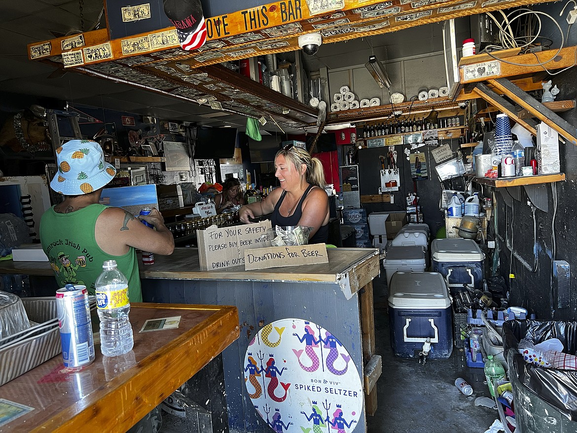 Ashley Galassi, a bartender at Tina’s, a watering hole at Fisherman’s Wharf in Fort Myers, Florida, attends to a patron on Friday, Oct. 7, 2022. She says the bar will likely be demolished and reopen elsewhere. Hurricane Ian might have come and gone, but it has done long-term damage to the small businesses of a region heavily dependent on tourists and seasonal residents. (AP Photo/Bobby Caina Calvan)