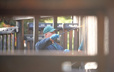 Mark Walter, city of Coeur d'Alene employee, sprays stain at Fort Sherman Playground at City Park on Friday. The city stains the wooden structures every other year. Panhandle Kiwanis Club members volunteered to help with the two-day project that began Thursday.