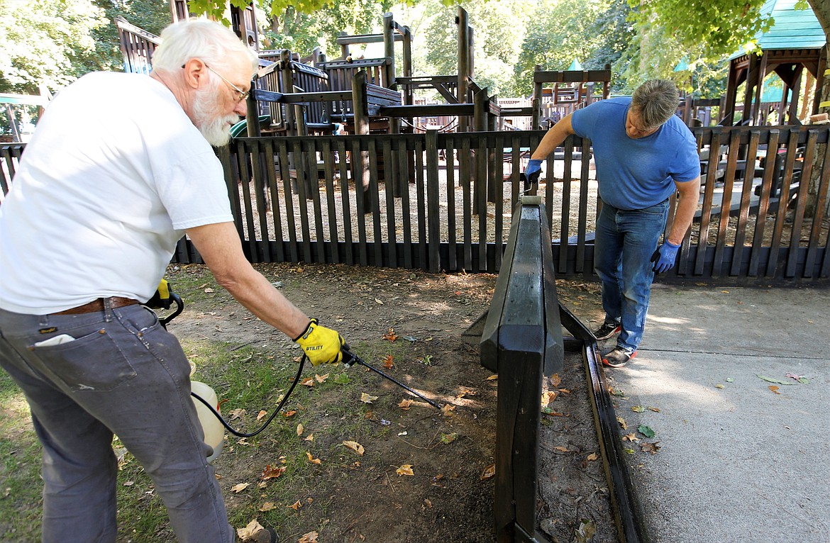 Wayne Koski, left, and Jon Dohm, volunteers with the Panhandle Kiwanis Club, stain the bike rack at Fort Sherman Playground at City Park on Friday. The city stains the wooden structures every other year. Panhandle Kiwanis Club members helped with the two-day project that began Thursday.