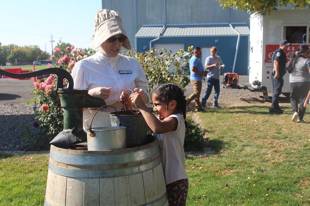 Bethany Cosio works to lift that heavy pail of water, with encouragement from volunteer Cassi Nelson in period costume.