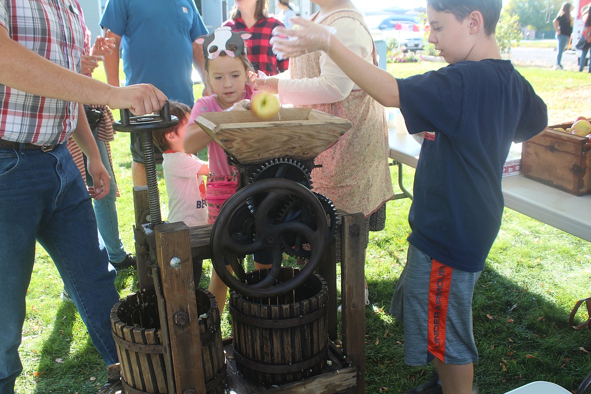 Mimi Alcala, back, turns the crank on the apple press, while Sawyer Golay, right, feeds the apples through.