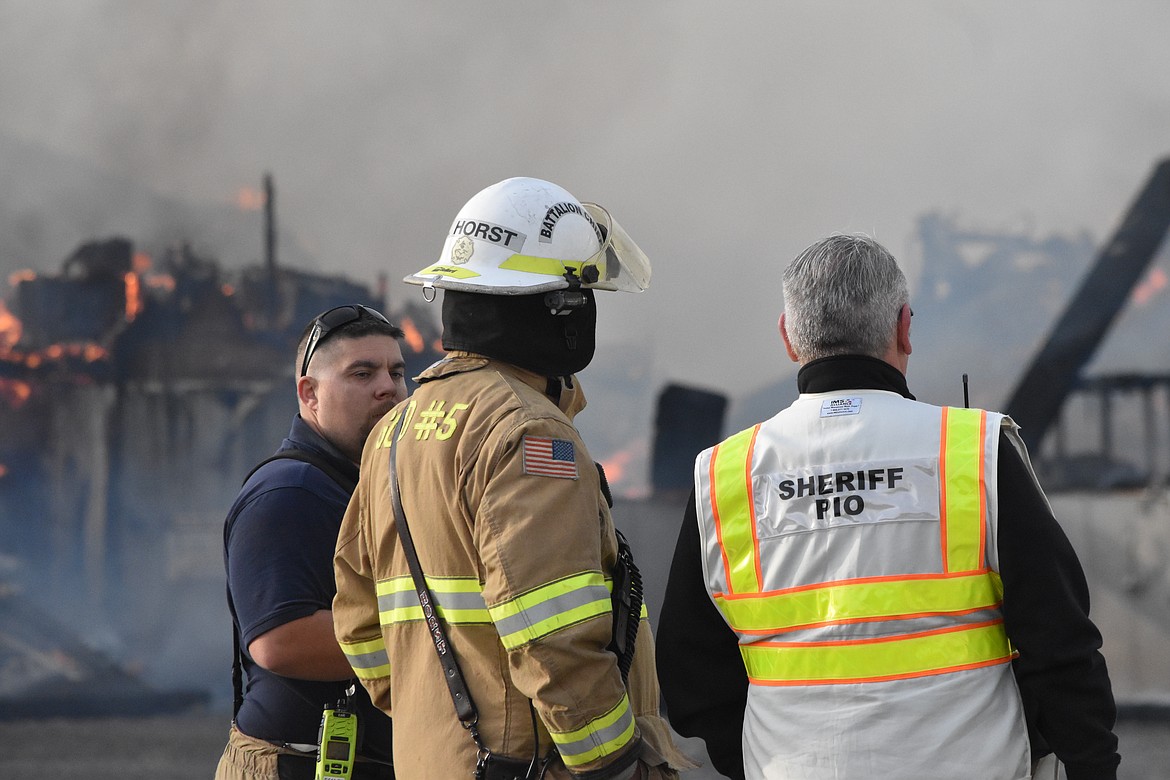 Grant County Public Information Officer Kyle Forman, right, speaks with Grant County Fire District Battalion Chief Robert Horst, middle, and another GCFD5 firefighter as smoke billows from the fire at the Wilbur-Ellis plant.
