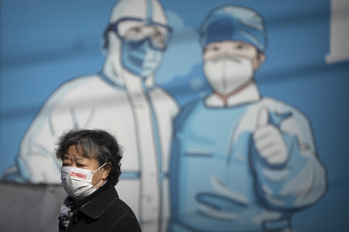 A woman wearing a face mask walks past a mural depicting epidemic control workers in protective suits in Beijing, Tuesday, Nov. 1, 2022. Shanghai Disneyland was closed and visitors temporarily kept in the park for virus testing, the city government announced, while social media posts said some amusements kept operating for guests who were blocked from leaving. (AP Photo/Mark Schiefelbein)