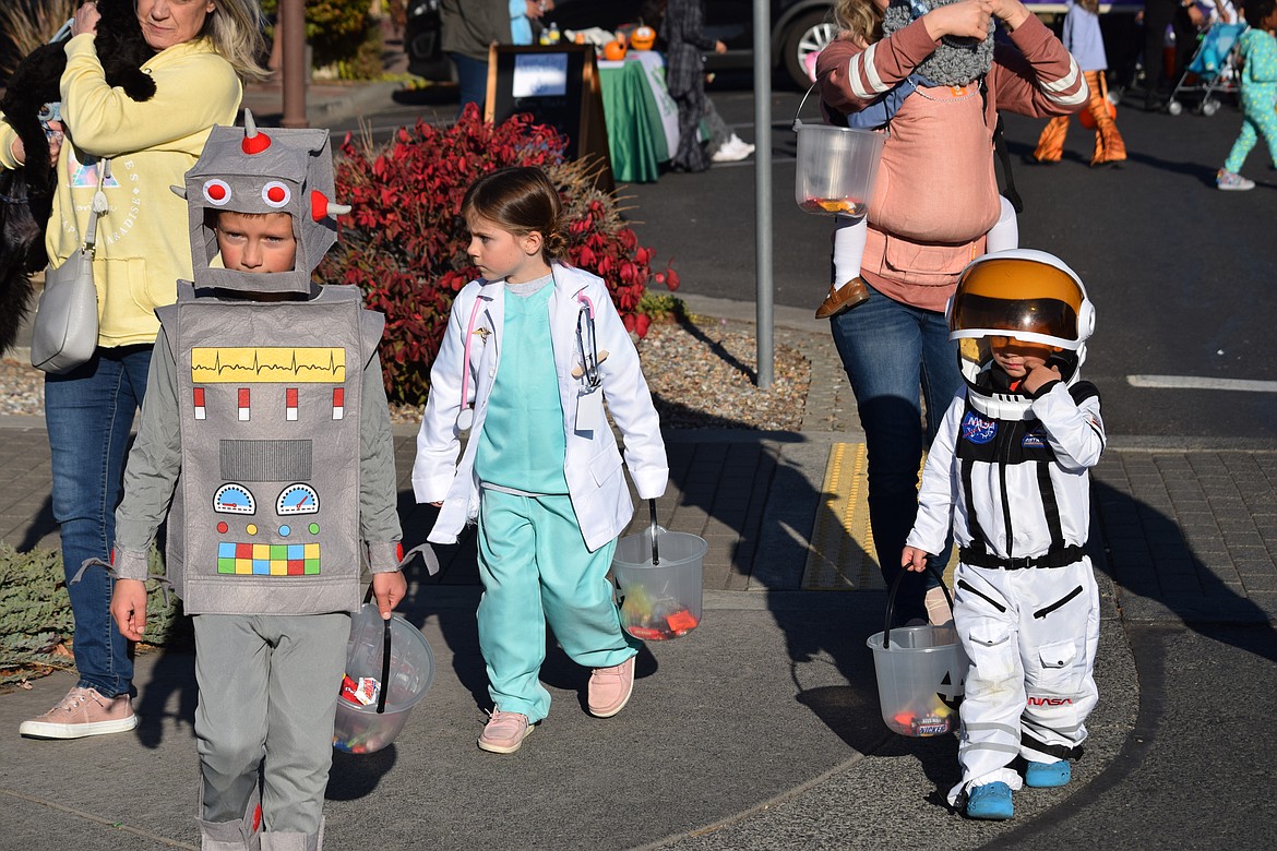 Trick-or-treaters Carson Conway, the robot, and his sister Carter, the doctor, and Lincoln, the astronaut, walk down Third Avenue in-between trunk-or-treat sites during the Harvest Festival on Saturday.