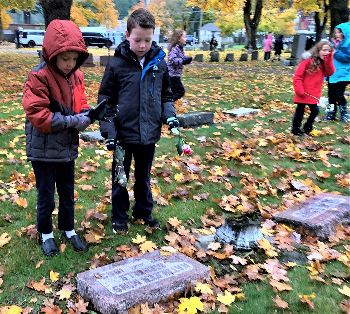 Holy Family Catholic School students Barney Spooner, left, and Christian Matheson stop at a headstone at St. Thomas Catholic Cemetery on Wednesday.