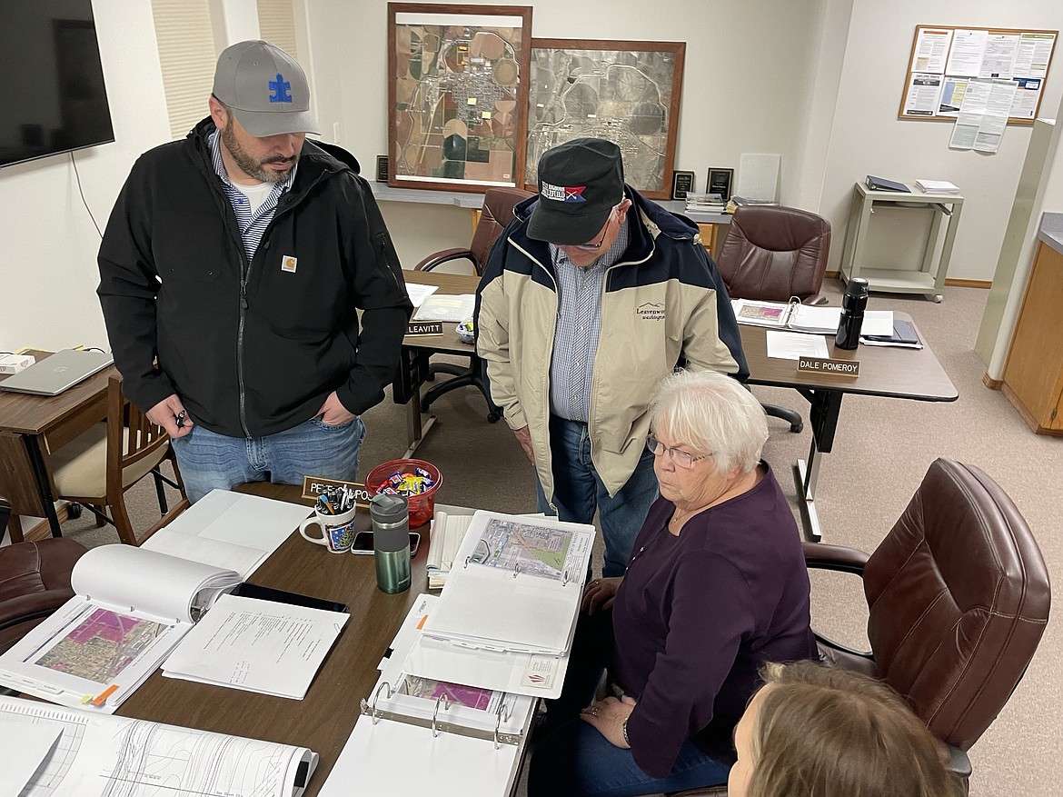 Port of Warden commissioners Pete Campos (standing, left) and Dale Pomeroy (right) look at a notebook of port properties open in front of Executive Director Pat Millard as they discuss how best to get road access to port property on the west side of Warden.