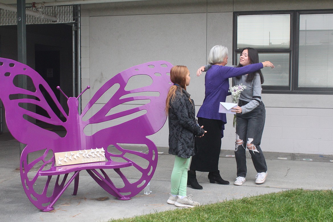 Lana Redal, in purple, gives a hug to Alicia Diaz, right, who designed the bench in honor of Redal’s granddaughter Ella Moungmany. Ella’s friend Penelope Smiley, front, was part of the dedication ceremony.