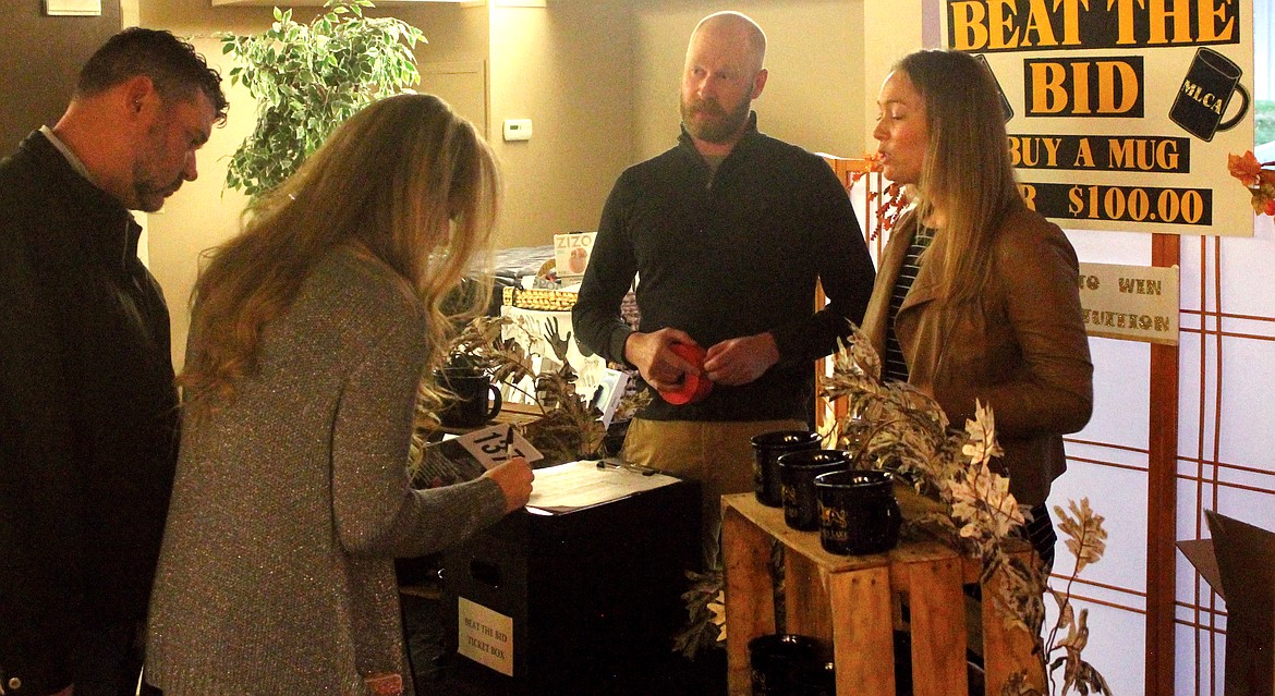 Michael and Katharina Rainis, right, explain the Beat the Bid fundraiser to Lance and Ashley Seitz at the Moses Lake Christian Academy dinner and auction Saturday. Purchasers paid $100 for a mug and entry in a raffle. The winner could choose between half a year’s tuition or a staycation at the MarDon Golf Course.