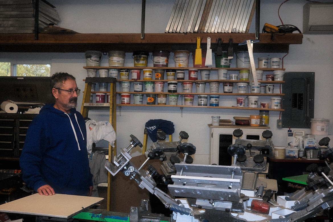 Troy Schweigert stands by printing equipment in his garage, home of Shirt Shack Screen Printing in Evergreen. (Adrian Knowler/Daily Inter Lake)