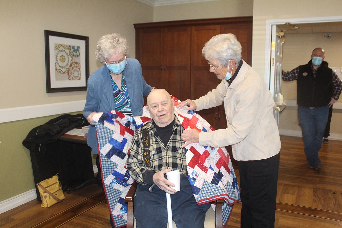 Basin Piecemakers Guild members Nancy Latham (left) and Karen McGhghy (right) drape a quilt over the shoulders of military veteran Bob Busherd. Guild members make quilts and donate them to veterans throughout the year.