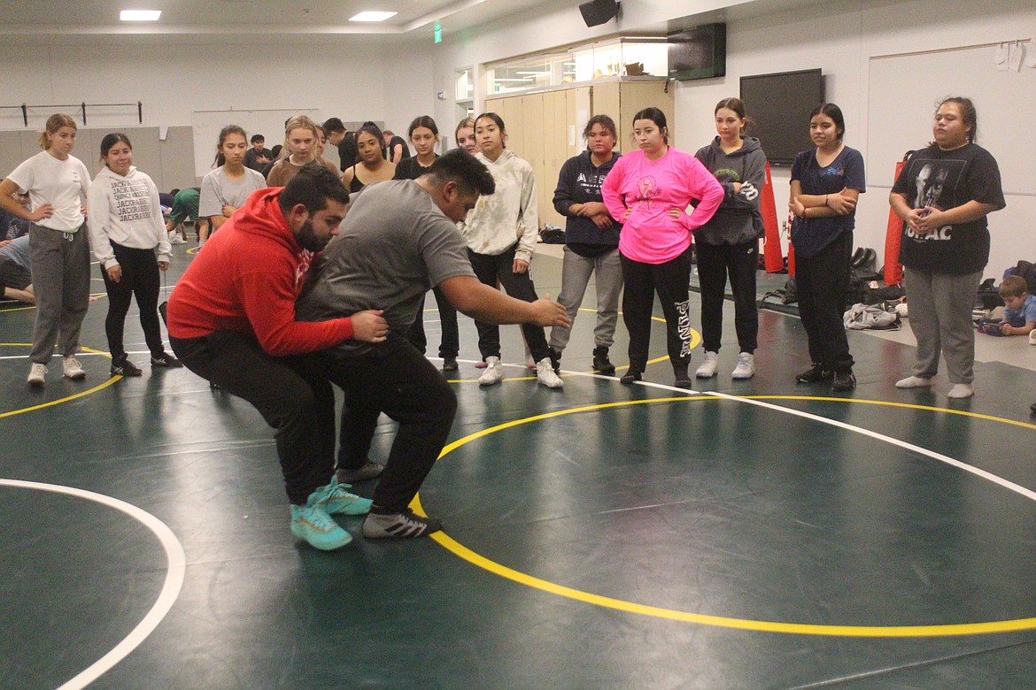 Quincy wrestling coaches Devan Silva (in red) and Antonio Melendez (in gray) demonstrate a move for the QHS girls wrestling team during practice.