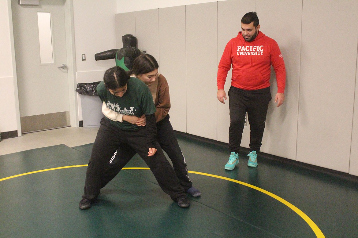 Head girls wrestling coach Devan Silva (in red) coaches a pair of wrestlers on their technique during Quincy High School practice.