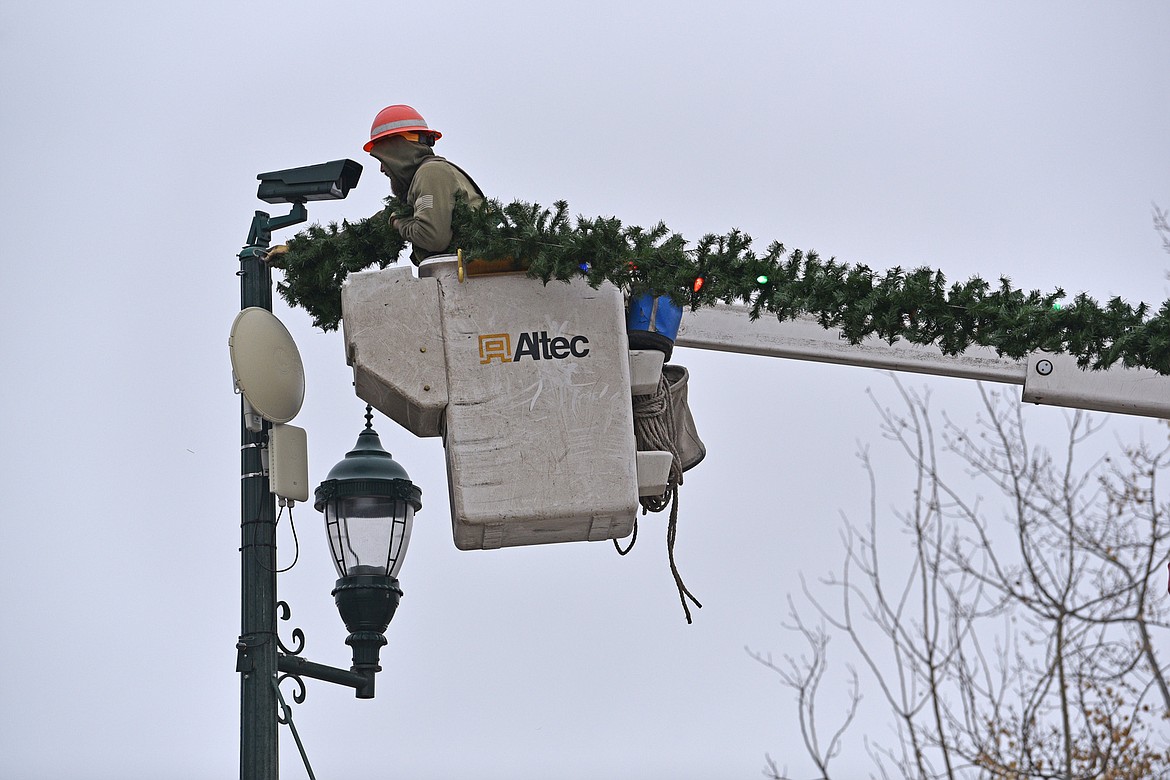 A member of the FEC crew connects a garland to a street light on Sunday morning in Whitefish. (Julie Engler/Whitefish Pilot)