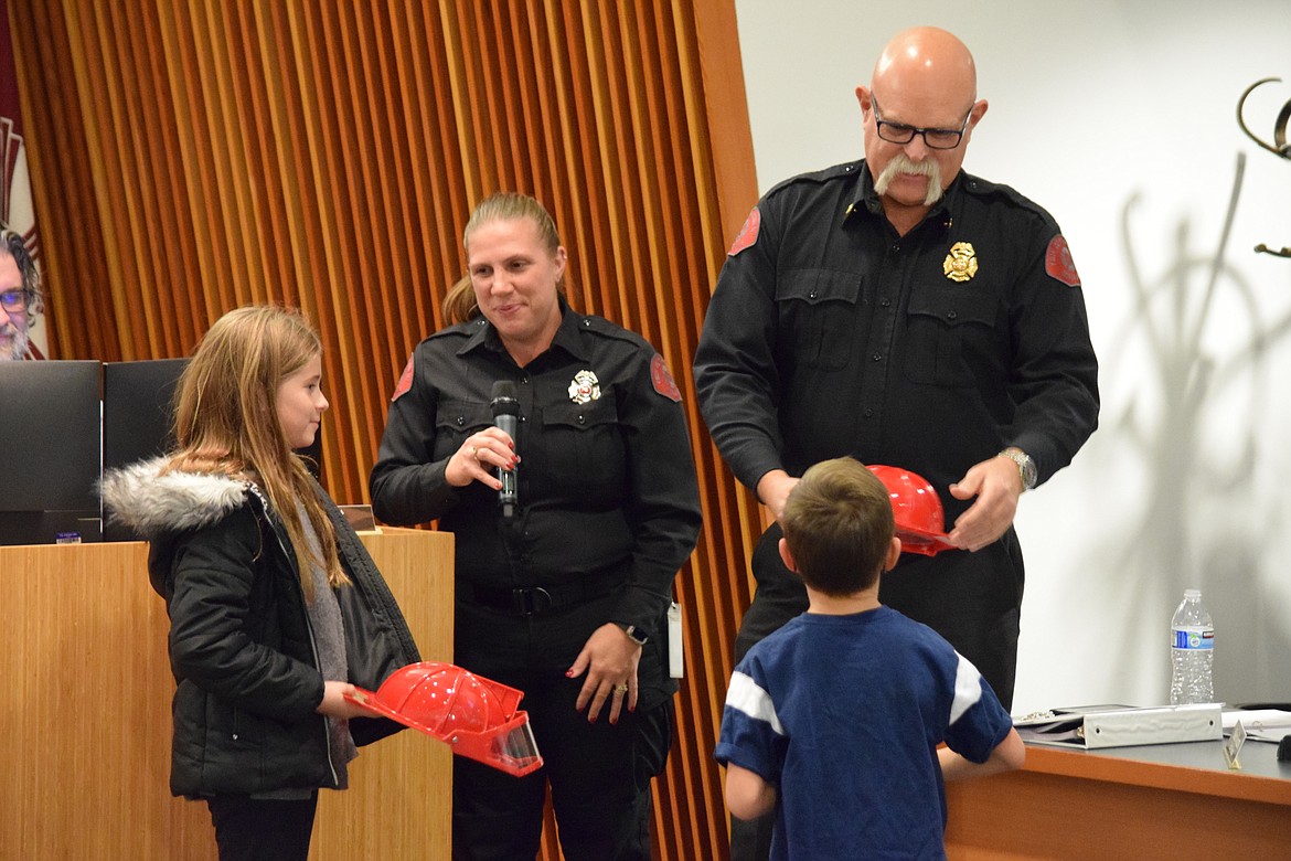 Moses Lake Fire Department Administrative Coordinator Heidi Merritt (left) and Chief Brett Bastian (right) give special helmets to Olive and Joshua Hardy at a regular city council meeting on Tuesday to thank the two children for spotting a house fire in early November and alerting their parents.