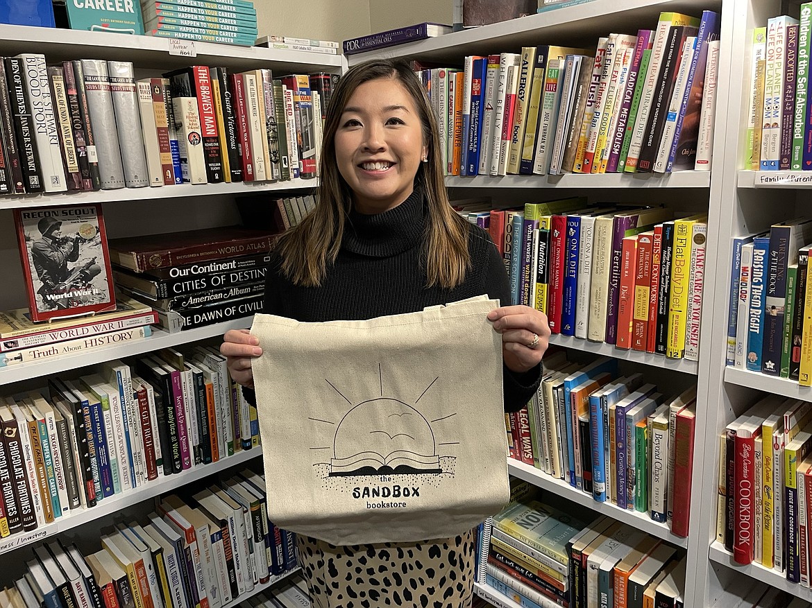 Mai Houvener, owner of Sandbox Bookstore in downtown Moses Lake, shows off one of the cloth carrying bags she sells in the revamped bookstore, which has a wide selection of used books, new books, games and even harmonicas.
