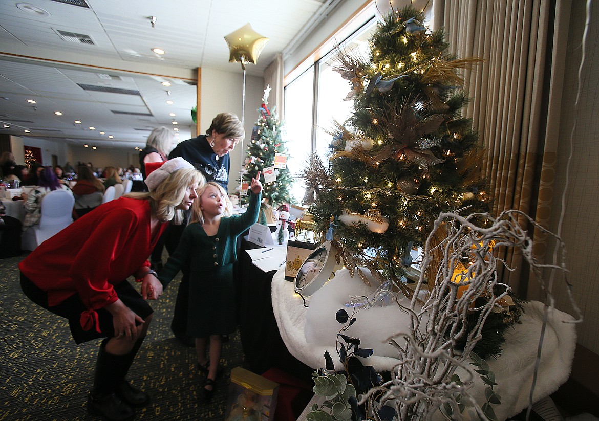 Emily Clark, wearing a Santa hat, inspects a Cinderella-themed tree that caught her 5-year-old daughter Emma's eye Saturday morning during the Post Falls Chamber's 2022 Post Fallidays Tiny Tree Festival in the Red Lion Hotel Templin's on the River.