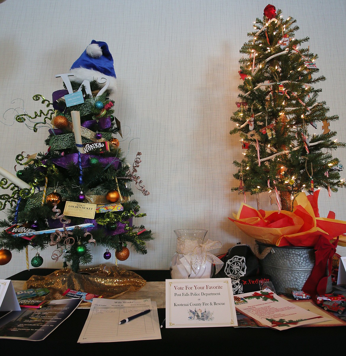 Guests at the seventh annual Post Fallidays Tiny Tree Festival in Post Falls on Saturday cast their votes for the Post Falls Police Department's Willy Wonka tree, left, or for Kootenai County Fire and Rescue's firefighter Christmas tree in a friendly people's choice competition.