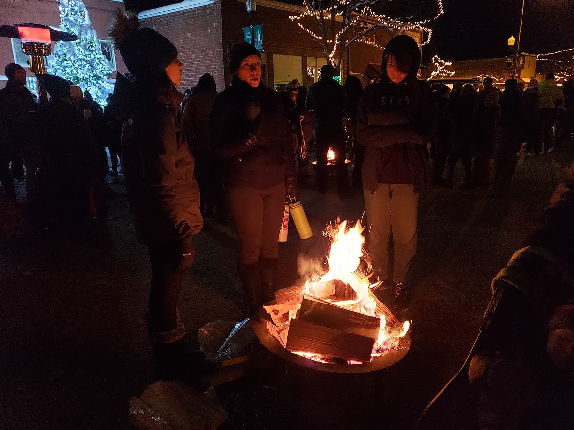 Zoe Drake, left, Jennifer Drake, center, and Zamora Flack warm their hands around one of the fire pits placed Saturday along Main Street in Rathdrum during the town's holiday festivities.