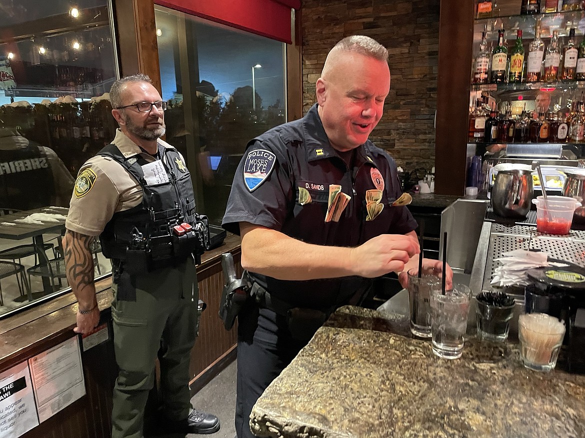 Moses Lake Police Department Capt. David Sands, standing in front Grant County Sheriff’s Office Chief Deputy for Investigations Gary Mansford, prepares a glass of water for a customer during the Tip-A-Cop fundraiser on Wednesday.