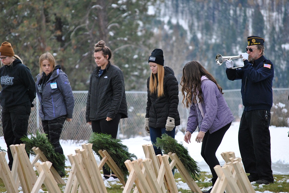 St. Regis student, Lilly Sansom places a handmade wreath on a wooden marker during the Pearl Harbor Remembrance ceremony last Wednesday, as Scott Burrows of the St. Regis Ray Welch American Legion Post plays Taps. (Mineral Independent/Amy Quinlivan)