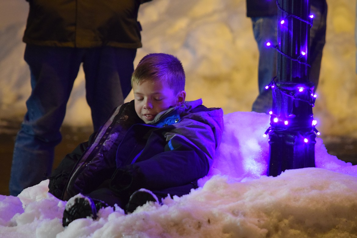 A boy sits in a snow drift along Basin Street in Ephrata waiting for the Bells on Basin parade on Saturday.